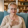 Older woman meditating with headphones on, sitting peacefully on a sofa at home