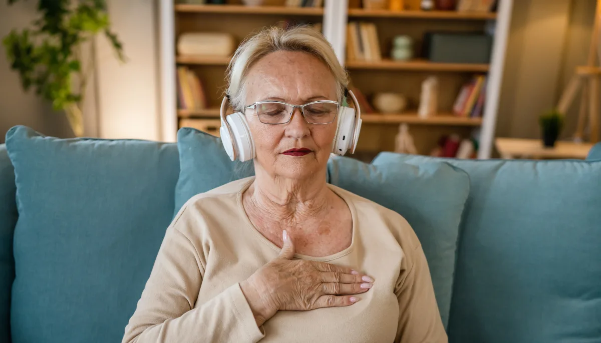 Older woman meditating with headphones on, sitting peacefully on a sofa at home